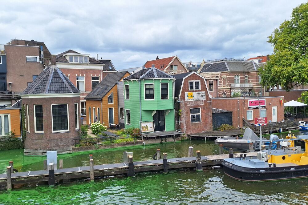 Gekleurde huizen aan het water van de Achterzaan in Zaandam, met een boot ervoor